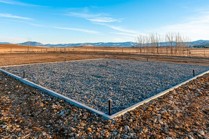 Compacted gravel pad with concrete anchor perimeter as cheapest foundation for a steel building